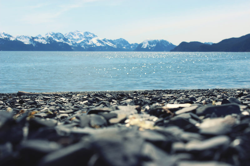 Shingle beach, with the first snow on the far side of the water.