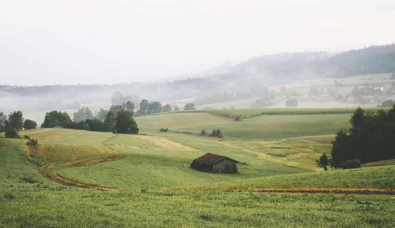 A barn, a field, and the hills going grey behind them.