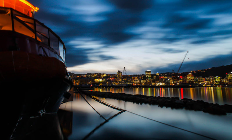 A ship tied up for the night, lights coming on across the water.